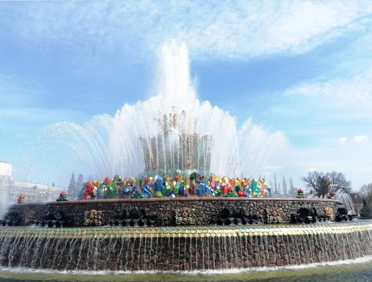 The colourful sculptural composition of the Stone Flower fountain behind tall jets of water.