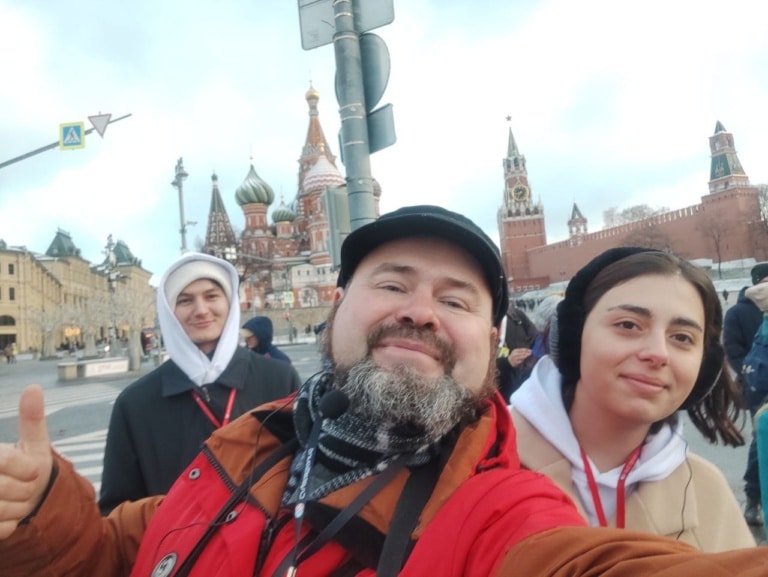 Гид Алексей делает селфи с участниками экскурсии на фоне храма Василия Блаженного