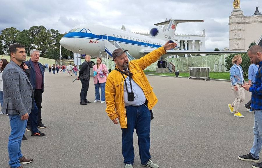 Экскурсия с гидом Алексеем по территории ВДНХ. На заднем плане виднеется Як-42 Гид Алексей показывает участникам ВДНХ. Як-42 на заднем фоне