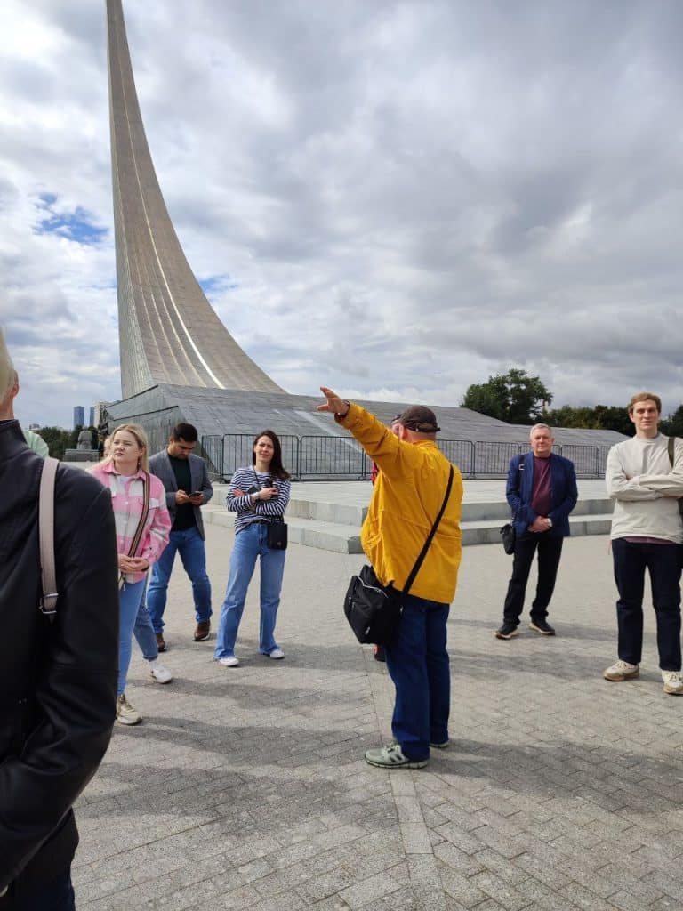 Гид Алексей с участниками на фоне стеллы Покорителям космоса