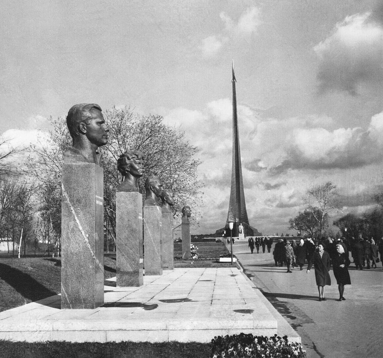 Чёрно-белая фотография Аллеи Космонавтов: слева ряд бюстов, вдали обелиск с ракетой, по дорожке идут люди.