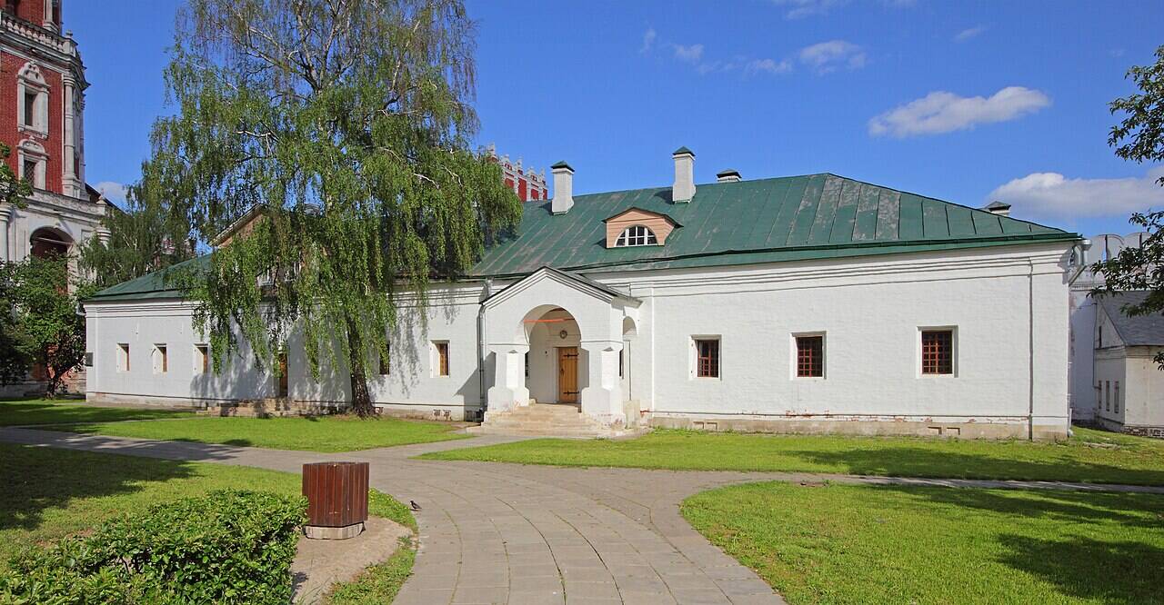 Белое одноэтажное здание Больничных палат с зелёной крышей и входным крыльцом.