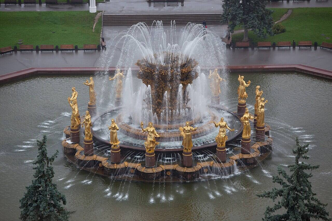Вид сверху под углом на фонтан «Дружба народов»: золотистые женские фигуры стоят по кругу вокруг работающей чаши.
