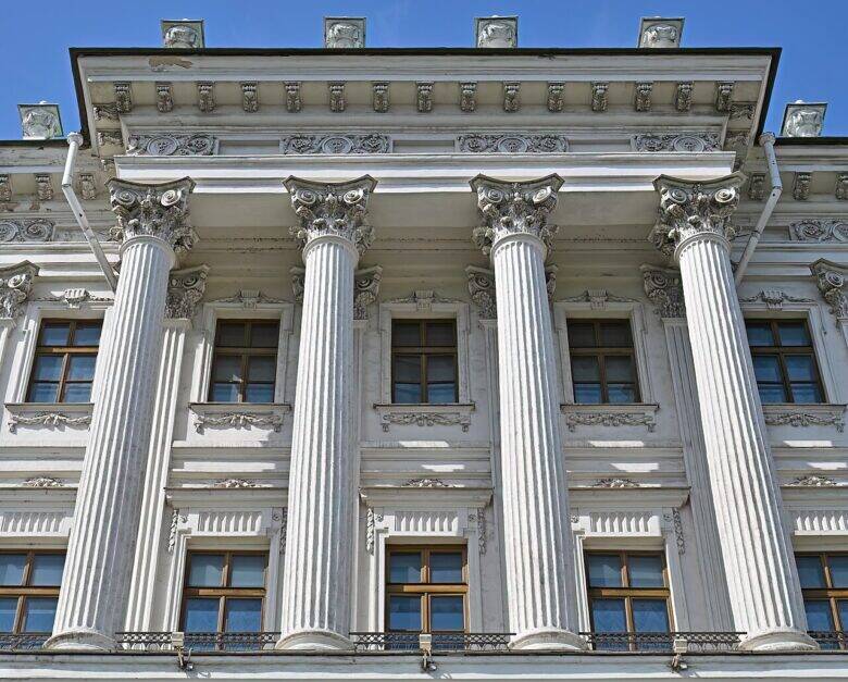 Четыре колонны Дома Пашкова с украшенными капителями; за ними видны окна и декор фасада.