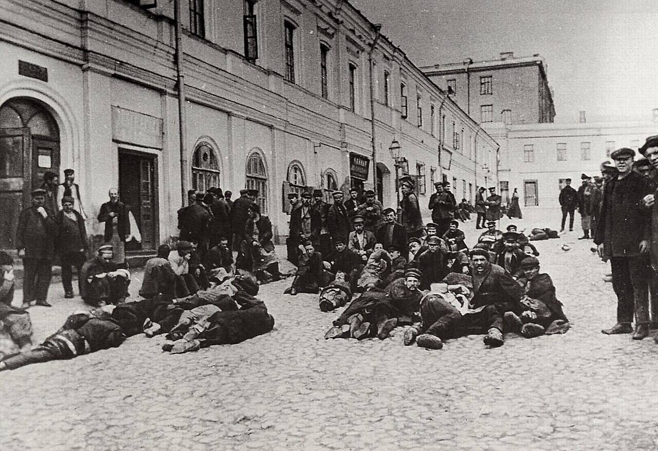 Обитатели ночлежек Хитровской площади сидят и лежат на мостовой у здания в Москве в 1904 году