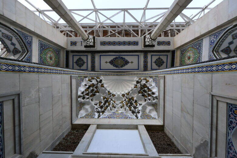 A glazed hall in the pavilion with ornamented walls, patches of exposed earth and a rectangular depression in the centre.