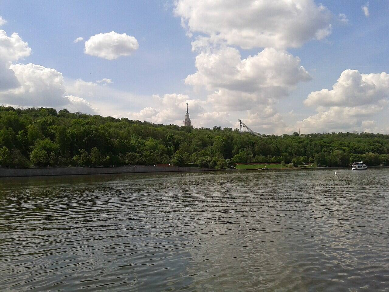 The Moscow River in the foreground, with the wooded slope of Sparrow Hills beyond; the spire of Moscow State University and a ski jump rise above the trees.