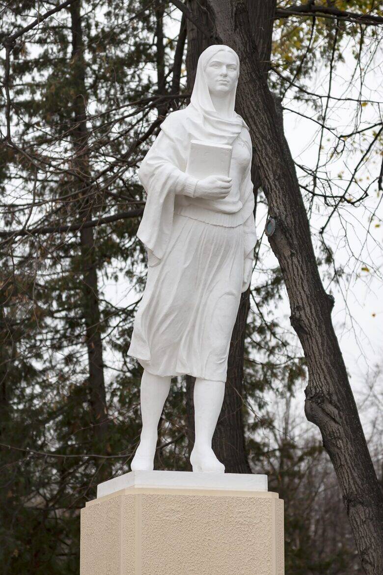 A white sculpture of a woman wearing a headscarf and holding a book, standing on a pedestal beside the Azerbaijan Pavilion.