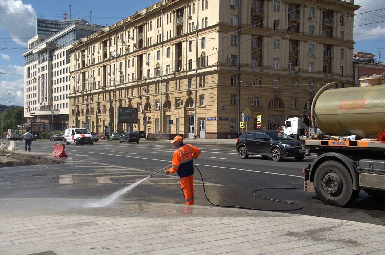A residential building at the corner of Novy Arbat and Novinsky Boulevard, with a road worker and a street-watering truck in front