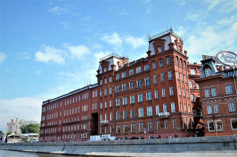 A red-brick factory building with a long wing and a tall central section along the embankment.