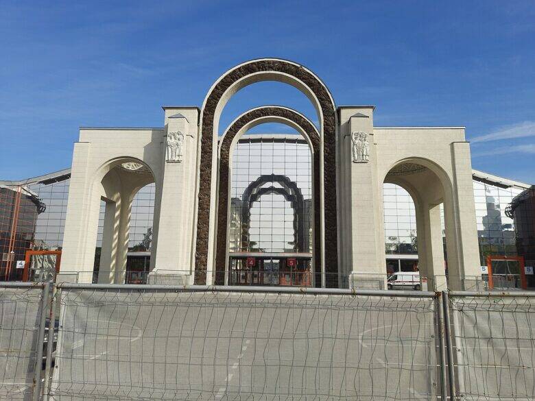 Front view of the light-coloured North Entrance arch at VDNKh, with a metal fence in front.
