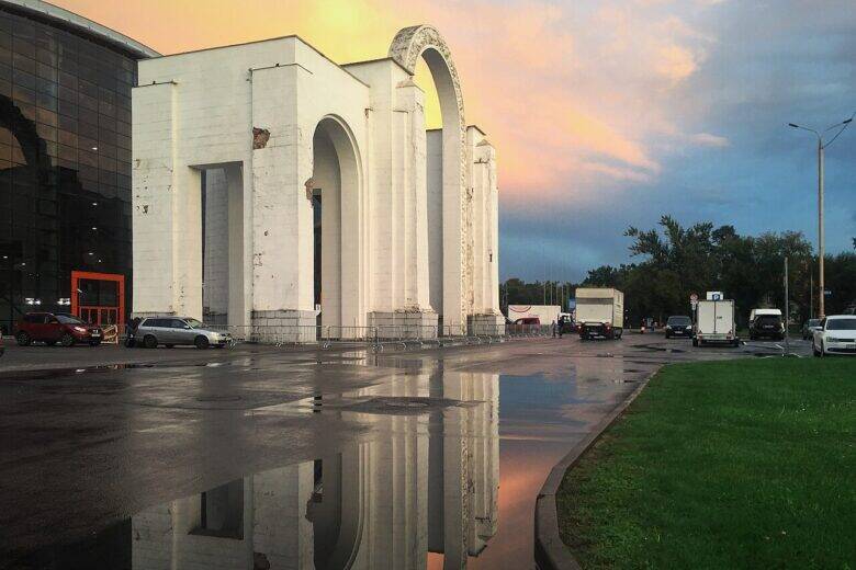 The white North Entrance arch at VDNKh, with its tall openings, against the evening sky