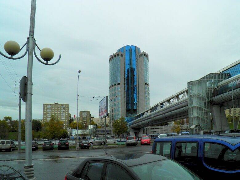 Цилиндрическая Башня 2000 за остеклённым мостом с диагональными металлическими элементами; внизу автомобили.