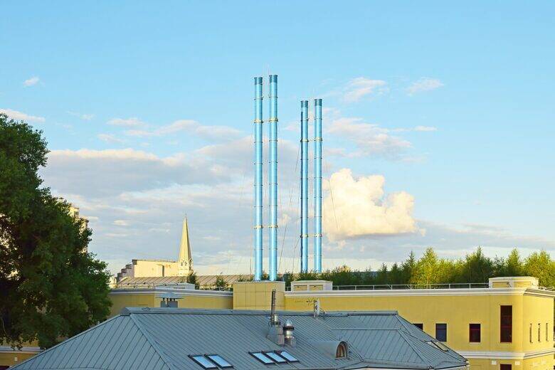 Four tall light-blue chimneys above pale roofs; trees and a spire on the left.