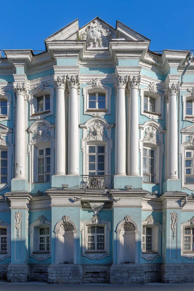 Центральная часть бирюзового фасада с белыми колоннами, лепниной, нишами и светлым цоколем.