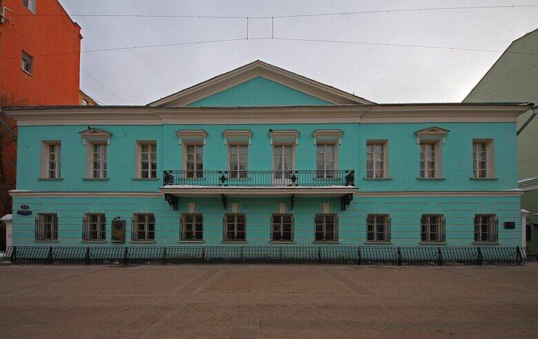 A blue two-storey house on Arbat, with a triangular pediment and a wrought-iron balcony.