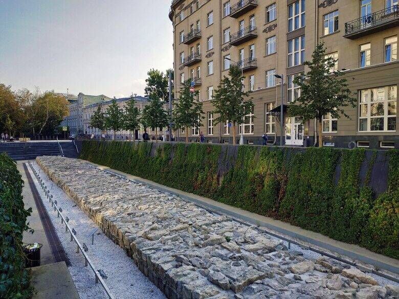 A long section of masonry in a sunken amphitheatre, with a landscaped slope and houses visible above.