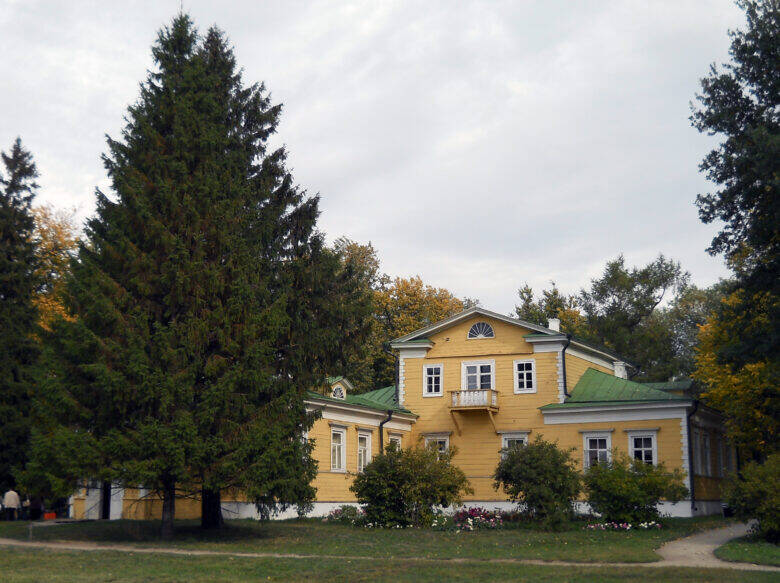 The yellow manor house on the Pushkin family estate, with a mezzanine and balcony, set among trees.