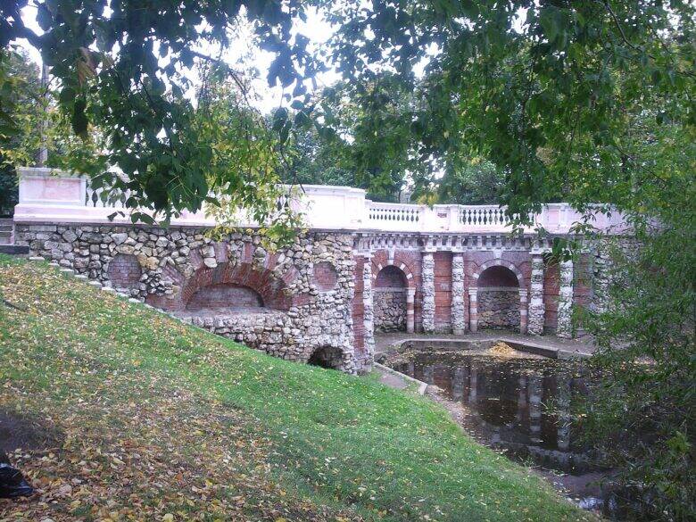 A stone and brick grotto with arched niches and a pale balustrade beside the water in Lefortovo Park