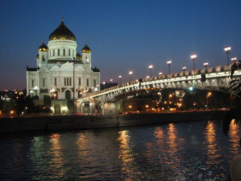 The illuminated Cathedral of Christ the Saviour and Patriarshy Bridge over the Moskva River at dusk.