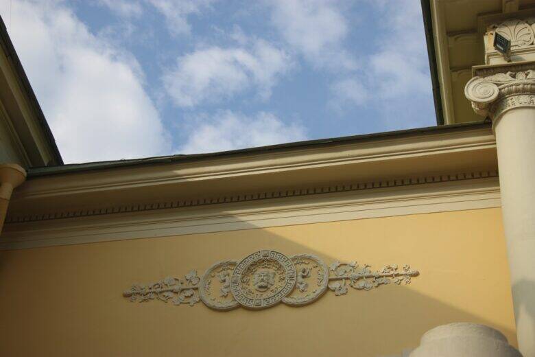 A white plaster medallion with floral ornamentation on a yellow wall; part of a column is visible on the right.