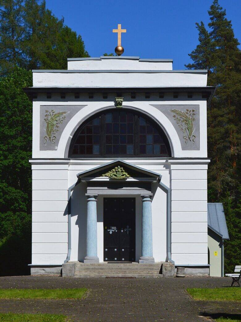 The white façade of the mausoleum, with an arched window, columns at the entrance and a cross on the roof.