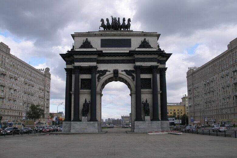 Триумфальная арка в Москве с тёмными колоннами и колесницей наверху, снятая прямо спереди.