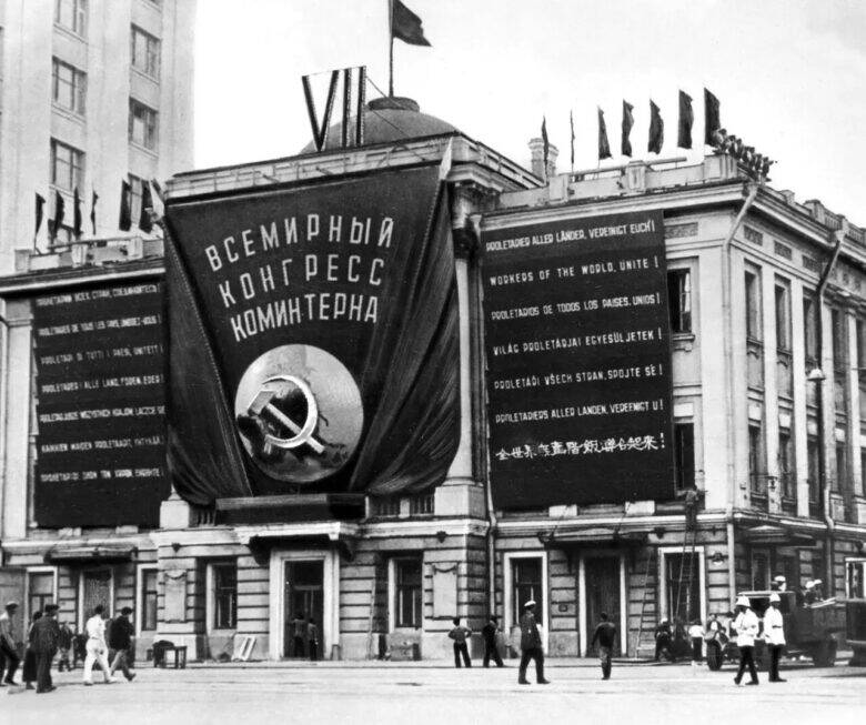 Фасад Дома Союзов с полотнищем «ВСЕМИРНЫЙ КОНГРЕСС КОМИНТЕРНА», серпом и молотом; перед зданием идут прохожие.
