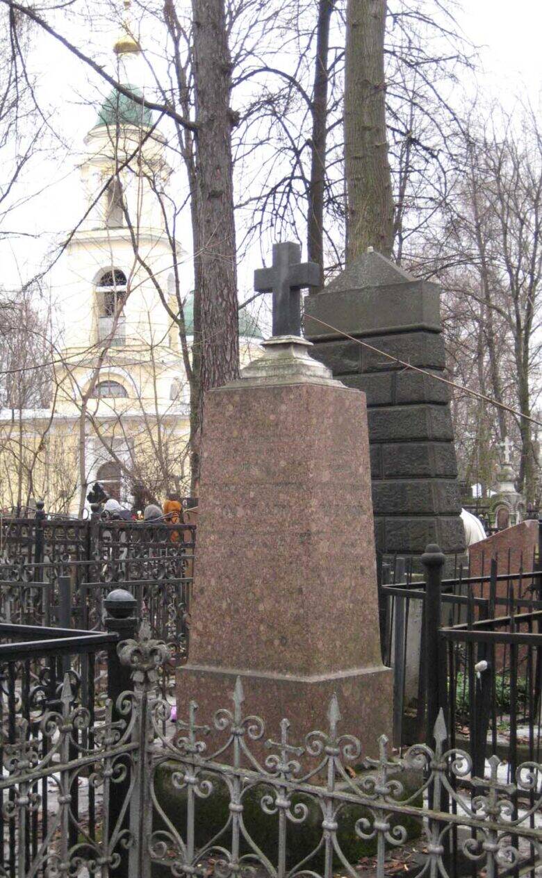 A stone gravestone with a cross behind a metal fence at Vagankovskoye Cemetery