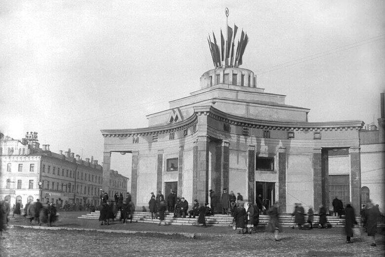 Архивная фотография павильона метро «Арбатская»: у входов идут люди, над крышей возвышается декоративная конструкция.