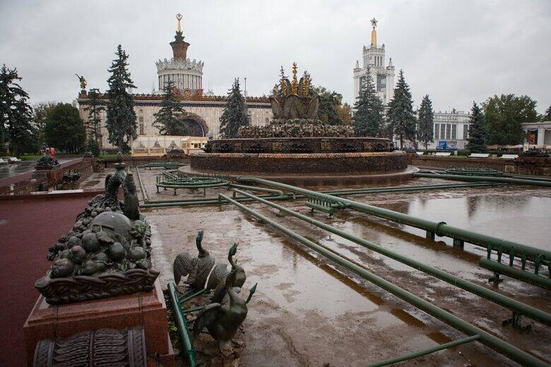 The drained pool of the Stone Flower fountain with exposed pipes; a sculpture on a pedestal stands in the left foreground, with the main sculptural composition in the centre.