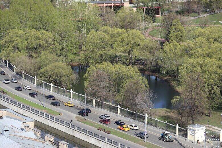 An aerial view of the Oval Pond among the trees in Lefortovo Park; cars travel alongside a white fence.