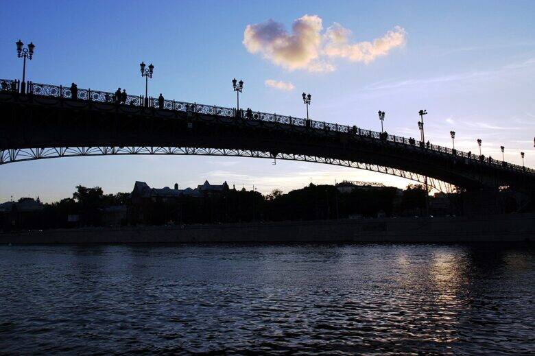 A side view of Patriarshy Bridge over the Moskva River: the silhouette of the span, railings and lamps against the evening sky.