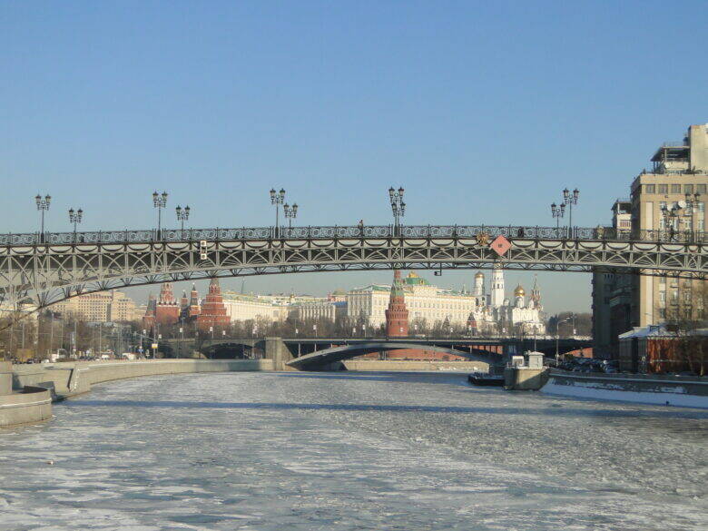 The latticework of Patriarshy Bridge over the ice-covered Moskva River; Bolshoy Kamenny Bridge and the Kremlin are visible behind it.