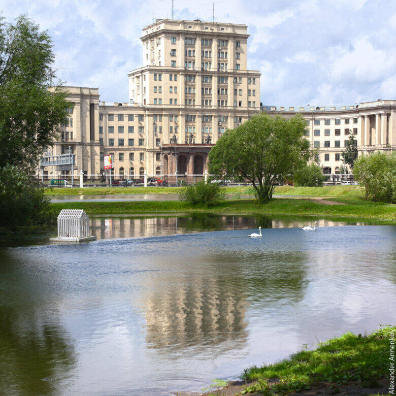 A pond with birds on the water and grassy banks; the main building of Bauman Moscow State Technical University rises behind the trees.