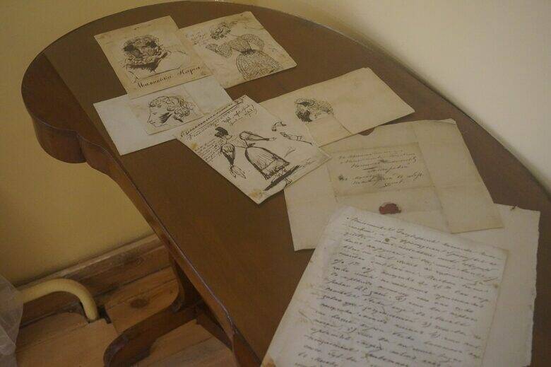 Several drawings, an envelope with a seal and a handwritten sheet lie on a wooden table in the museum.