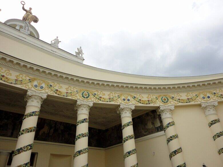 The curved colonnade of the Belarus Pavilion at VDNKh and the mural behind the decorated columns.