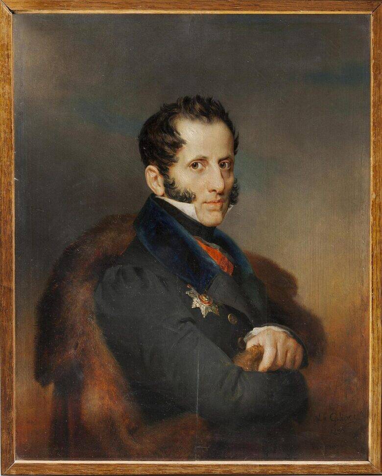 A man in dark clothing wearing an order of merit sits partly turned towards the viewer and looks out at them; a framed painted portrait.
