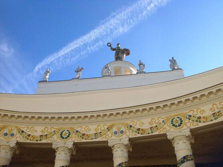 Light-coloured sculpted figures above the curved colonnade, with a golden figure on the rotunda above them.