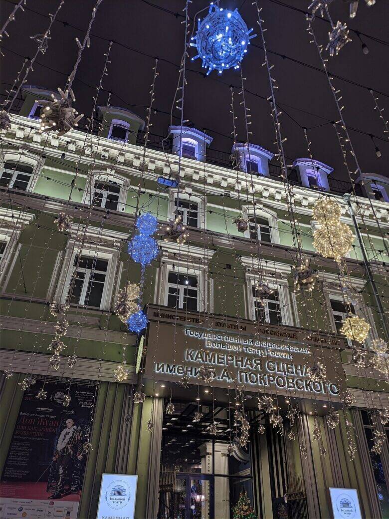 The façade at 17 Nikolskaya Street illuminated in the evening, with a sign for the B. A. Pokrovsky Chamber Stage and festive garlands.