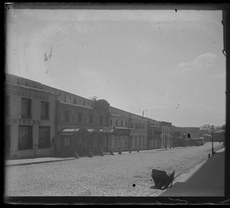 An archival view of cobbled Staraya Square: a row of buildings with signs on the left and a handcart in the foreground.
