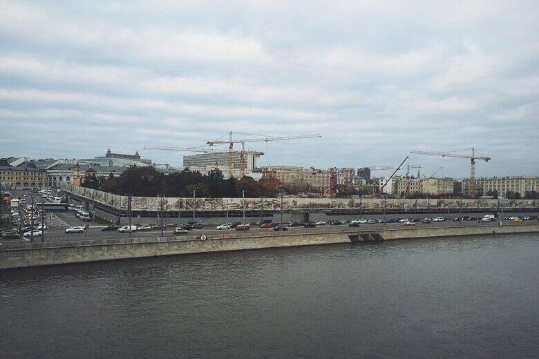 A view across the Moskva River towards the embankment and a construction site with cranes.