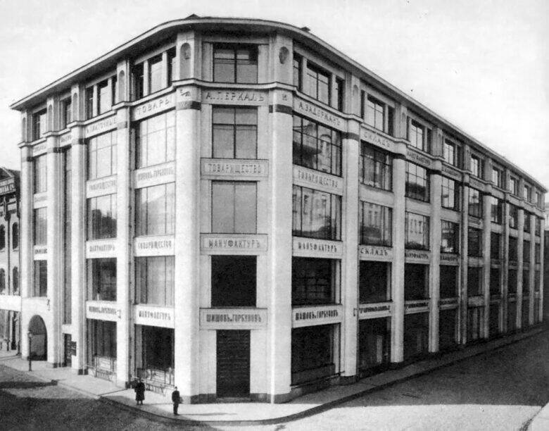 An archival view of a commercial building with a rounded corner, rows of large windows and signs on the façade.