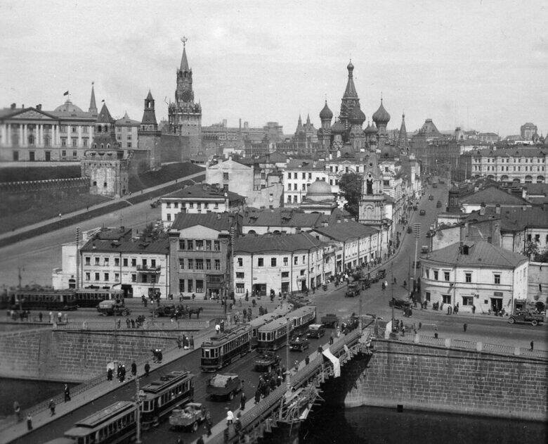 Black-and-white panorama: trams on the bridge, densely packed city blocks beyond it, the Kremlin wall on the left and the domes of the Cathedral of the Intercession in the distance.