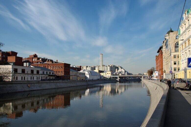 A view along the Vodootvodny Canal: brick buildings and two tall chimneys on the left, the stone slope of the embankment and a road on the right.
