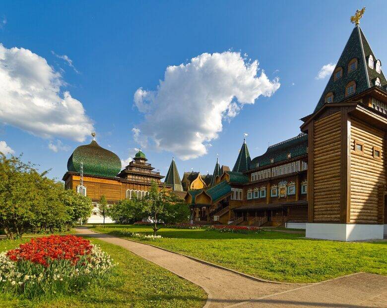 The wooden palace at Kolomenskoye with green tented roofs and a dome; a path and flower beds in the foreground