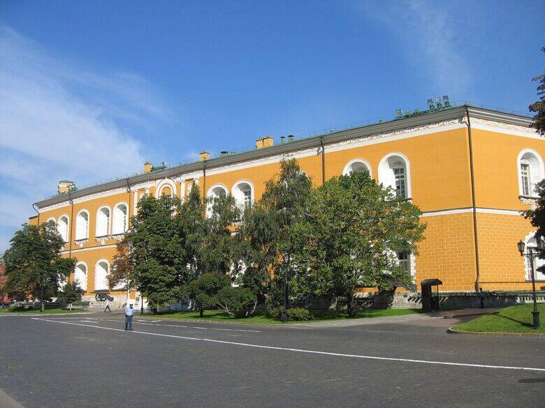 The Arsenal’s long yellow façade with two rows of arched windows; trees and a road in front of the building.